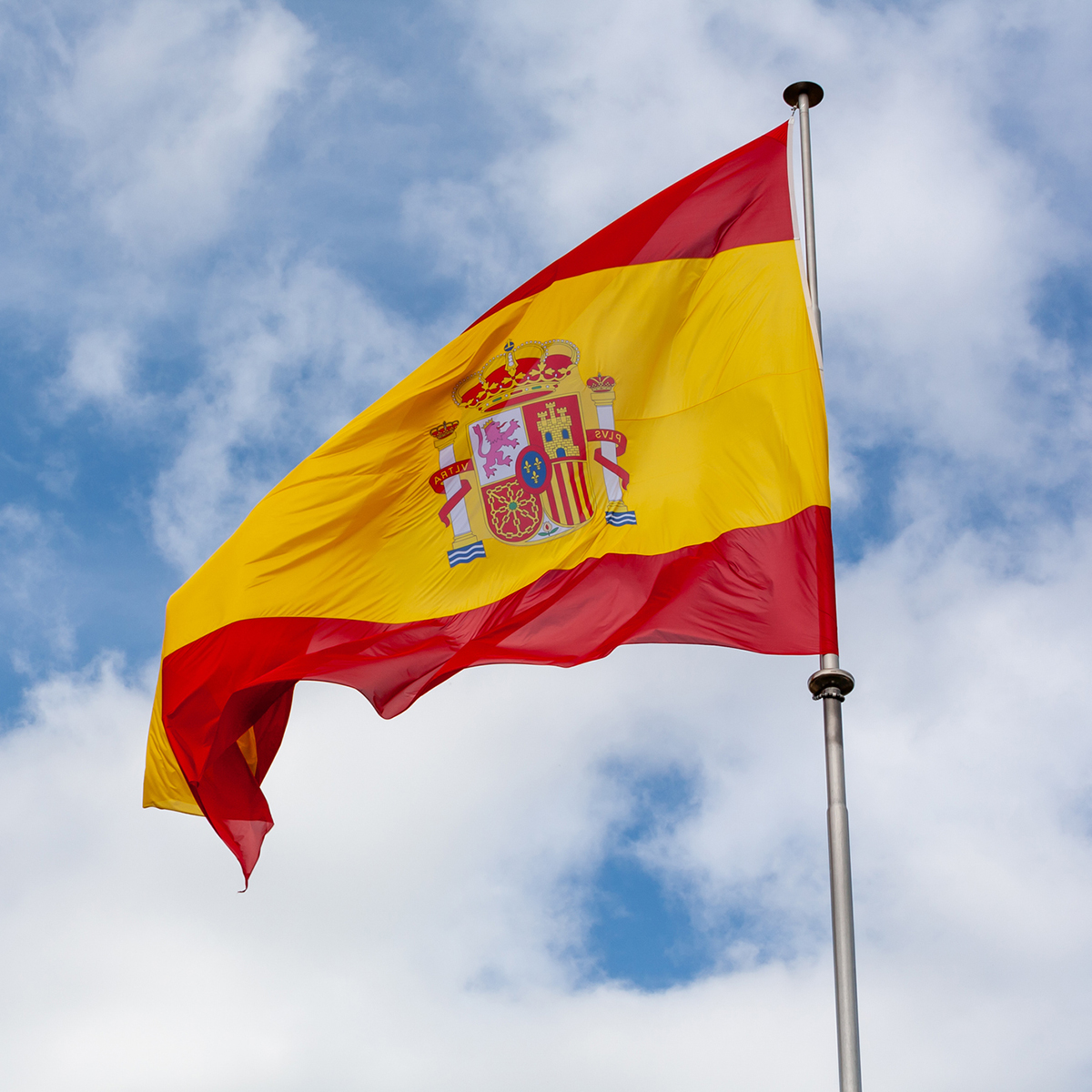 A vibrant national flag with red, blue, and symbolic elements waves against a clear sky, representing a European country.