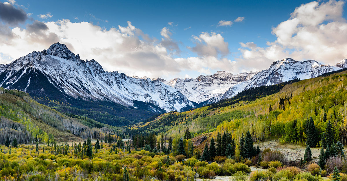 Vue panoramique d'une large vallée boisée, avec des montagnes enneigées à l'horizon.