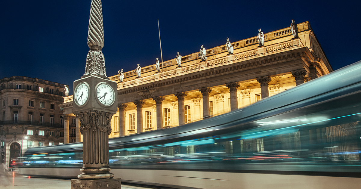 Landscape photo of a European city, highlighted by a prominent clock tower, an imposing and palatial government building, and an above-ground metro transit train moving at high speed